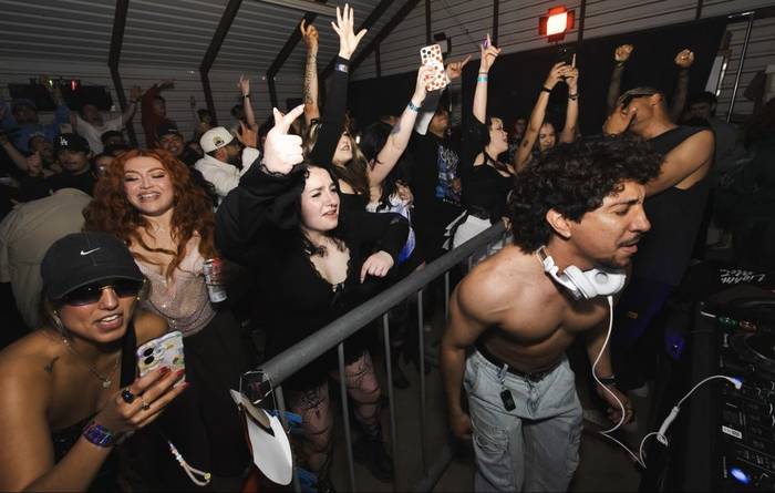 The front row on the rail, hands up, phones out, a red spotlight in the rafters