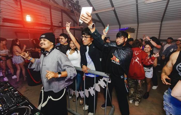 Friends at the rail, one holding a paper sign over the crowd, red light behind