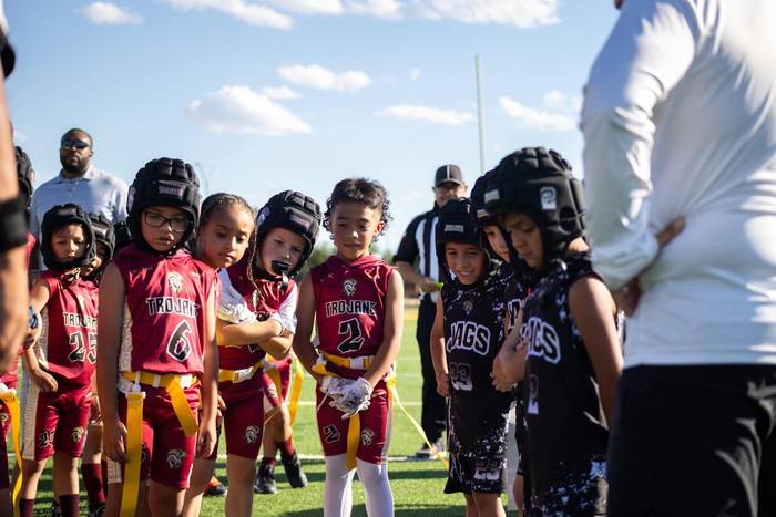 A youth flag football team in maroon and gold at the sideline, helmets on, waiting on the coach